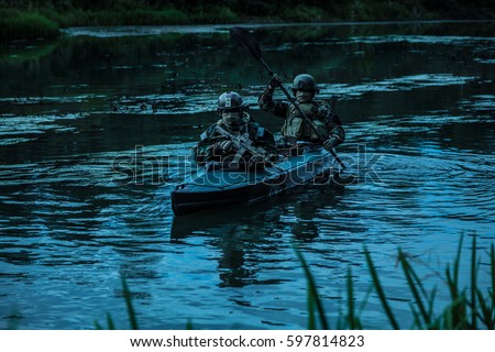 Special forces men with painted faces in camouflage uniforms paddling army kayak. Boat moving calmly across the river, diversionary mission, twilight