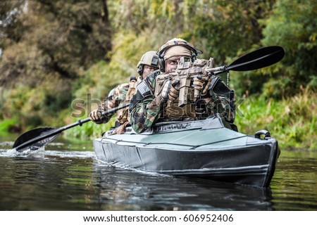 Special forces men with painted faces in camouflage uniforms paddling army kayak. Boat moving across the river, diversionary mission, front view
