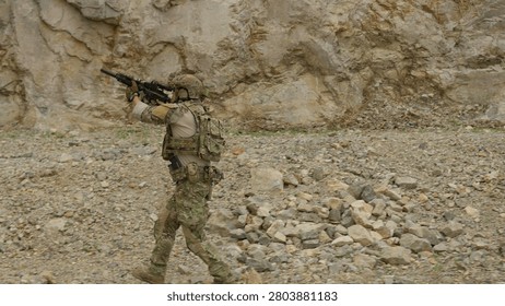 A special forces operator in full tactical gear maneuvers through rugged terrain during a military mission, maintaining combat readiness with an assault rifle.