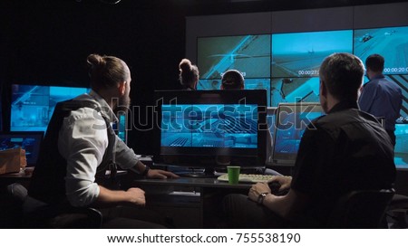 A special forces and policemen surveillance team in a modern office with large live screens.