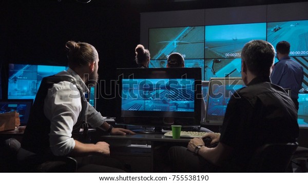 Une équipe de surveillance des forces spéciales et des policiers dans un bureau moderne avec de grands écrans en direct.