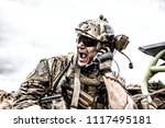 Special forces soldier, military communications operator or maintainer in helmet and glasses, screaming in radio during battle in desert. Calling up reinforcements, reporting situation on battlefield