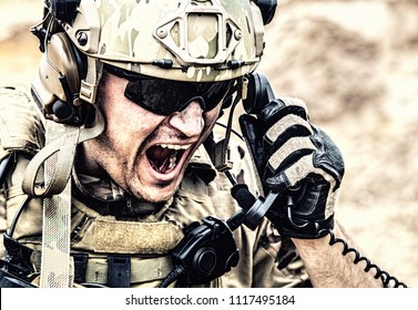 Special Forces Soldier, Military Communications Operator Or Maintainer In Helmet And Glasses, Screaming In Radio During Battle In Desert. Calling Up Reinforcements, Reporting Situation On Battlefield