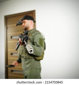 A Special Forces Soldier With A Rifle With A Silencer And A Night Vision Device On His Head During A Tactical Exercise In The House. Soft Focus, Main Focus On The Weapon.