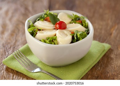 Special fresh salad of heart of palm (palmito), cherry tomatoes and basil in white bowl in center on rustic wooden background.