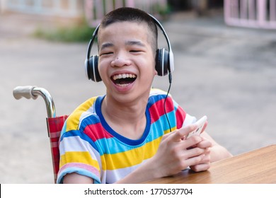 Special Need Child On Wheelchair Wear Headphones Use Smartphone And Smile Face,Study And Work At Home For Safety From Covid 19,Life In The Education Age Of Special Need Kid,Happy Disabled Boy Concept.