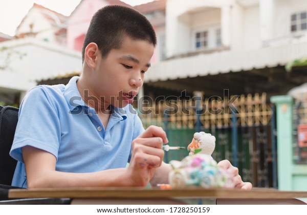  Special need child on wheelchair interested in\
skills development toy on home background,Education for disabled\
children style,Boy happy with plaster doll coloring, Happy\
disability kid concept.