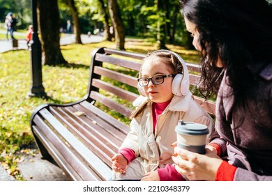 Special Need Child Wearing Headphones And Happy Time To Use A Smartphone On Bench With Her Mother In Park Outdoor.