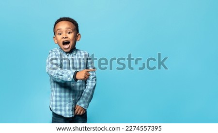Special offer. Adorable african american boy pointing his finger aside at copy space and looking at camera with open mouth, posing over blue studio wall, banner, panorama