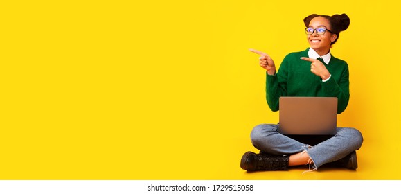 Special Offer. Excited black girl sitting on floor with laptop, pointing at copy space over yellow background. Panorama