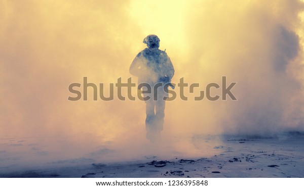 Special operations forces soldier, army ranger or\
commando in camo uniform, helmet and ballistic glasses walking at\
battlefield covered with smoke. Airsoft war game player coming\
through smoke screen