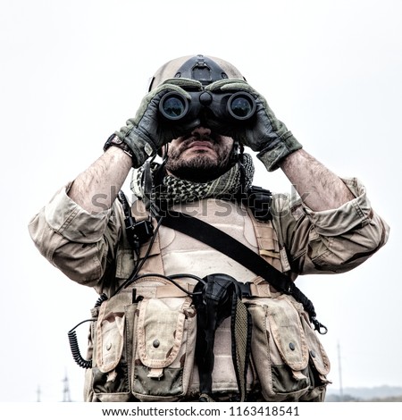 Special operations forces soldier, Navy SEAL scout in battle uniform and helmet, looking through binoculars, observing area, searching targets, monitoring enemy movements, directing artillery fire