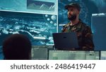 Special operations soldier allocating resources to different units based on mission needs, examines strategic data on a big screen in military control center. Marine corps troops. Camera A.