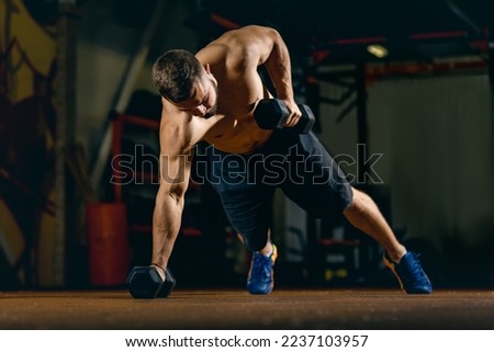 Special training equipment. Creating perfect body shape. Portrait of young sportive man doing push-ups with dumbbels, training in gym. Concept of sport, health, action, nutrition. Copy space for ad