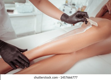 Special wax material. Attentive experienced cosmetologist working with wooden spatula while adding wax on the skin