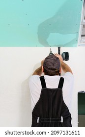 Specialist Assembles A Suspended Ceiling With Plasterboard. Assembly Process Using An Electric Screwdriver Plasterboard To The Metal Ceiling Frame. Simple And Affordable Renovation Of Premises