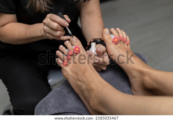 Specialist in a beauty salon giving a\
pedicure by painting toenails with glossy\
paint.