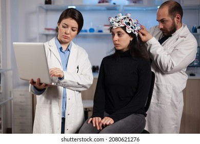 Specialist doctor holding laptop computer showing tomography to woman patient while neurologist man adjusting eeg scanner during neurology experiment. Team of researchers analyzing brain activity