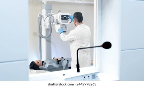 A specialist doctor in an X-ray room, a radiologist sets up a machine for radiography of a patient and makes a scan. The concept of medical technologies, modern medical equipment. - Powered by Shutterstock