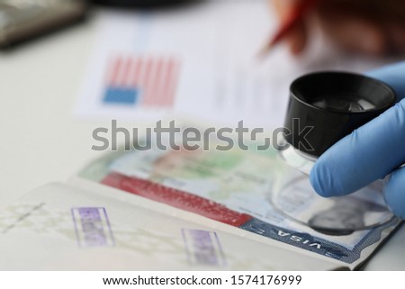 Specialist with loupe checking authenticity of american visa in passport close-up