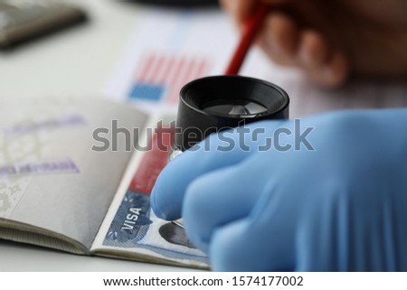 Specialist with loupe checking authenticity of american visa in passport close-up