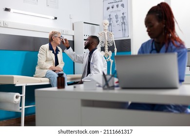 Specialist physician doctor man measuring temperature putting infrared thermometer on senior woman patient forehead discussing fever treatment. Medical appointment in hospital office. Medicine concept - Powered by Shutterstock