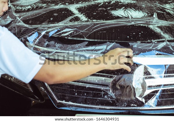 Specialist prepares car for protect against chips.Close
up of paint protection film installation on side bumper of modern
car.film applied to painted of car to protect the paint from stone
chips, 
