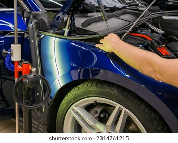 A specialist repairs a dent on the car body without painting. Process of paintless dent repair on car body. The mechanic at the auto shop with tools to repair dents in car body. Body repair. PDR.  - Powered by Shutterstock