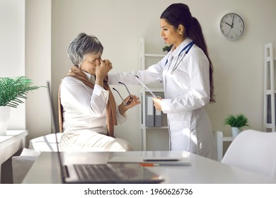 Specialist Supports Tired Stressed Ill Crying Older Adult Female Patient. Unhappy Troubled Senior Lady With Pain, Headache, High Eye Pressure, Bad Sight Or Blurry Vision Talking To Doctor At Hospital