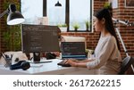 IT specialist types code on dual monitors in a cozy home office while working remotely. Asian woman uses programming language for productivity in coding and internet security. Camera B.