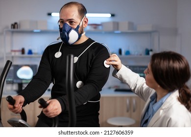 Specialist woman researcher putting electrodes sensor on sportman with mask monitoring EGK data in medical mordern laboratory. Athlete man running on fintess trainer working at body endurance - Powered by Shutterstock