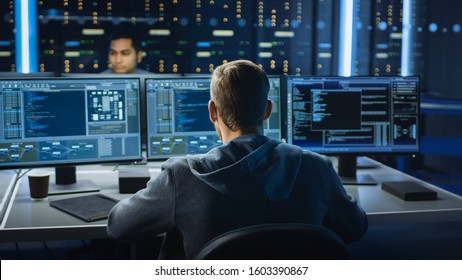 IT Specialist Works on Personal Computer with Screens Showing Software Program with Coding Language Interface. In the Background Technical Room of Data Center with Professional Working
