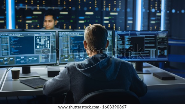 IT\
Specialist Works on Personal Computer with Screens Showing Software\
Program with Coding Language Interface. In the Background Technical\
Room of Data Center with Professional\
Working