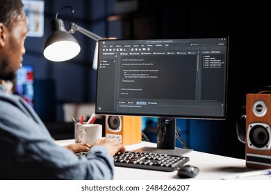 IT specialist writing html script binary code for database security, working on server optimization at home. African american hardware expert works on software programming, technical support.