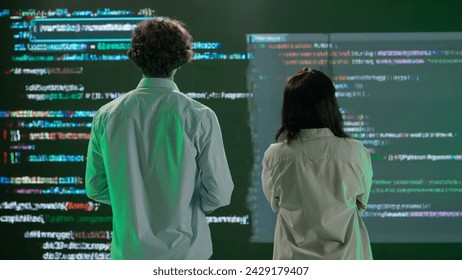 IT specialists against big digital screen. Back view of woman and man engineers stand in front of screen with digital code data error process
