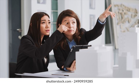 Specialists taking notes on tablet after reviewing building model, trying to capture accurate dimensions of physical spaces. Developers planning and designing architectural project. - Powered by Shutterstock