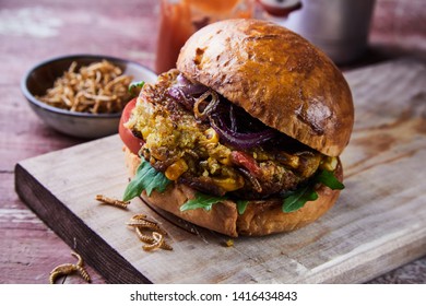 Speciality gourmet fried mealworm insect burger with salad trimmings on a fresh crusty bun served on a wooden board in a close up side view for a menu