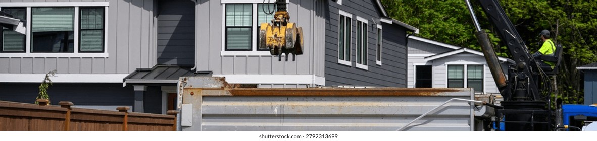 Specialized Grapple truck with operator using knuckle boom arm to empty construction waste dumpster into truck for transportation and removal, residential housing development project site
