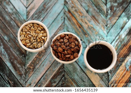Specialty coffee concept. Green raw coffee beans, roasted coffee beans and black coffee in three white cups on turquoise wooden parquet background top view