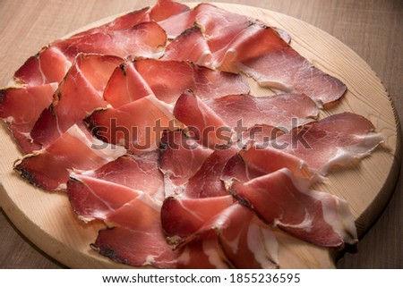 Speck, typical smoked ham from South Tyrol, Alto Adige in Italy - slices on wooden cutting board in top view