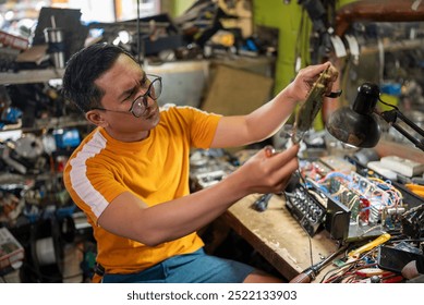 spectacled repairman working on electronic circuitry near a lamp at workshop - Powered by Shutterstock