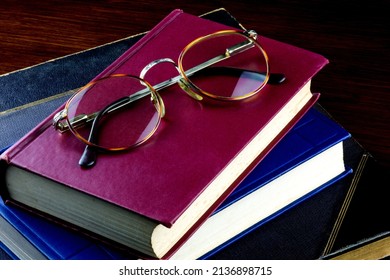 Spectacles with old books piled on a polished wooden surface