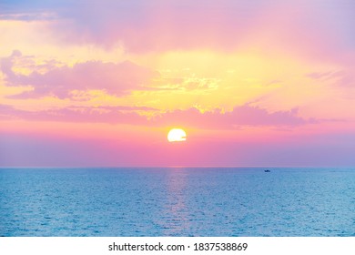 Spectacular beautiful sunset or sunrise on the mediterranean sea. Beautiful pink orange purple yellow light filters through the clouds. A small boat sails at the horizon on the turquoise sea - Powered by Shutterstock