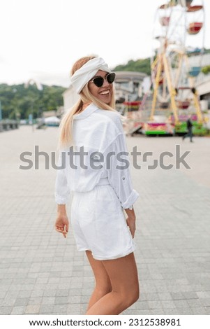 Spectacular charming cute lady with wonderful smile wearing white clothes turn around at camera and walking in the city . Close up portrait of stylish young woman in sunglasses smiling 