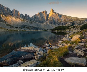 A spectacular cinematic view capturing the pristine glacial alpine waters of Drakolimni (Dragon Lake) on Mount Tymfi, with the immense limestone cliffs of the Astraka massif rising dramatically in the background. The image showcases the crystal-clear mountain tarn nestled within lush green highland pastures of the Zagori region. Located within the Vikos-Aoos National Park in Epirus, northwestern Greece, this iconic wilderness landscape is highly sought after for adventure tourism campaigns, trekking guidebooks, outdoor gear marketing, and premium travel editorials.