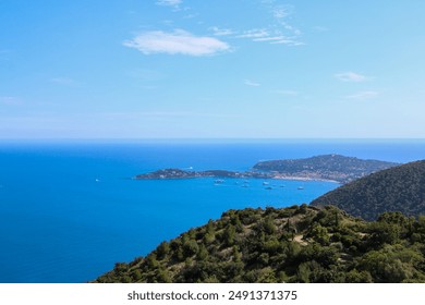 Spectacular coastal view featuring a vibrant blue sea, clear sky, and lush green hills. The scenic coastline includes a small island and scattered boats, offering a serene and picturesque seascape - Powered by Shutterstock