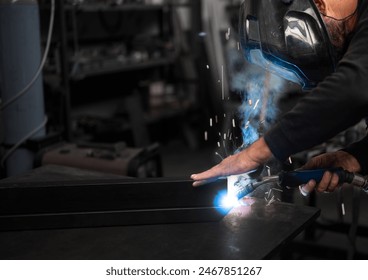 Spectacular conceptual image of a blacksmith busy using the welding machine. Sparks and smoke flash from the tip of the soldering iron. Blurred background. Welding, repair, work concept. Copy space. - Powered by Shutterstock