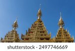 The spectacular roof of the temple against a clear blue sky. Pyramidal golden towers with openwork ornaments and carvings. Peaks on  rooftops. Dhammikarama burmese temple. Malaysia. Penang. Georgetown