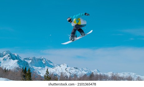 Spectacular shot of a snowboarding pro doing a rotating grab stunt while training in the scenic Vogel ski resort snowpark. Male snowboarder soars high through the air and does a breathtaking trick.