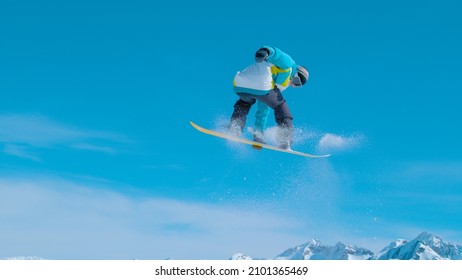 Spectacular shot of a young snowboarding pro doing a rotating grab stunt while riding in Vogel ski resort snowpark. Fit male snowboarder soars through the air and does a breathtaking snowboard trick.